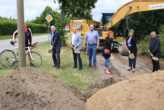 Mehrere Menschen stehen in einer Reihe und führen einen Spatenstich aus.