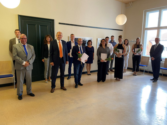 Die Absolventen sowie ihre Begleiter stehen mit Landrat Roger Lewandowski in einem Raum und schauen in die Kamera.