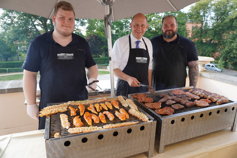 Drei Personen stehen hinter dem Grill - Klick öffnet Bildbetrachter