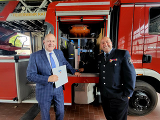 Zwei Personen stehen vor einerm Feuerwehrfahrzeug - Klick öffnet Bildbetrachter