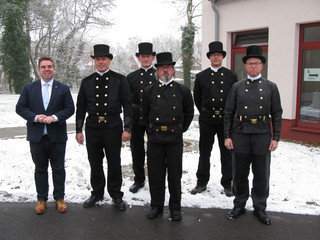 Sechs Männer, darunter fünf Schornsteinfeger stehen in einer Gruppe und schauen in die Kamera.