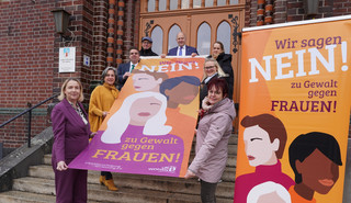 Klick öffnet Text; eine Gruppe von Menschen halten eine Fahne