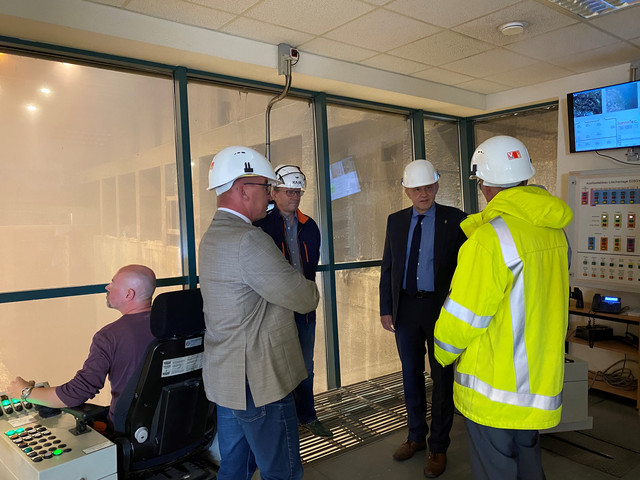 Vier Männer stehen im Kreis, im Hintergrund ist die Müllverbrennungsanlage zu sehen.