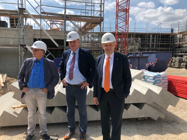 Drei Männer mit Bauhelm stehen auf einer Baustelle.