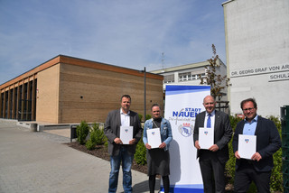 Vier Personen stehen vor einer Schule und halten jeweils eine Mappe in der Hand - Klick öffnet Bildbetrachter