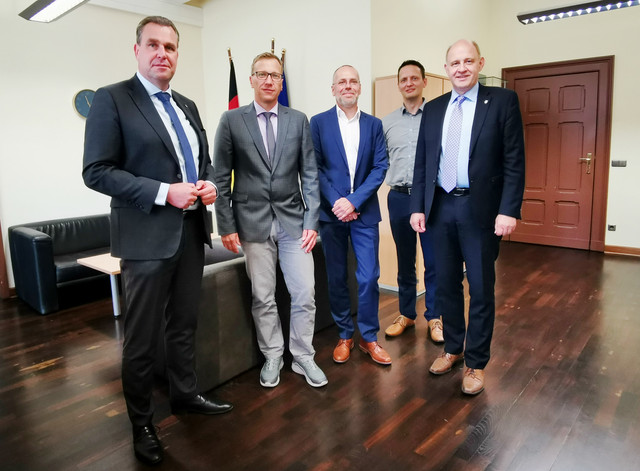 Fünf Männer stehen in einem Büro nebeneinander und schauen in die Kamera.