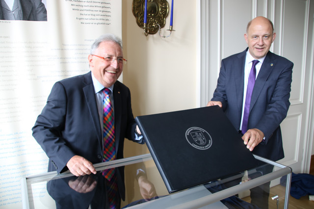 Kalligraph Bernd Thiel und Landrat Roger Lewandowski halten das neue Ehrenamtsbuch in die Kamera.