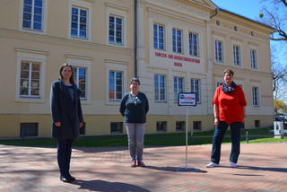 Drei Frauen stehen auf einem Platz, im Hintergrund ist das FGZ Nauen zu sehen.