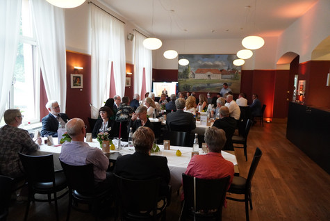 Blick in den Saal, wo die Gäste verteilt an mehreren Tischen sitzen und die Rede des Landrates an einem Bildschrim verfolgen - Klick öffnet Bildbetrachter