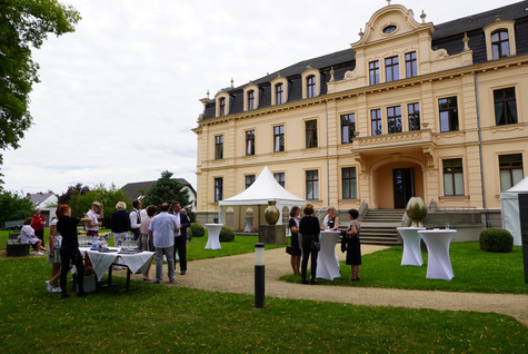 Gäste der Veranstaltung stehen verteilt auf einer Grünfläche vor dem Schloss Ribbeck - Klick öffnet Bildbetrachter