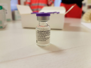 Eine Ampulle des Impfstoffes steht auf einem Tisch.