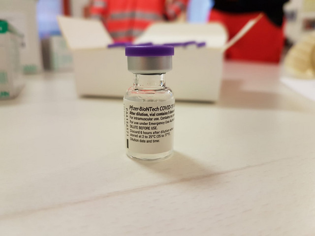 Eine Ampulle des Impfstoffes steht auf einem Tisch.