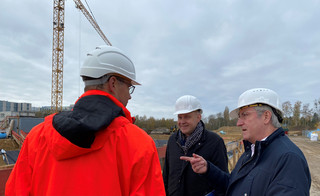 Drei Männer stehen auf einer Baustelle und unterhalten sich.