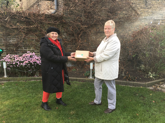 Zwie Frauen stehen im Garten, zwischen sich halten sie ein Päckchen.