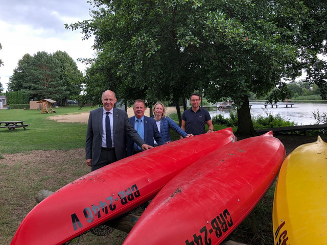 Vier Personen stehen hinter drei auf dem Kopf liegenden Kanu-Booten. Im Hintergund sieht man Wasser.