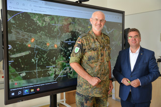 Zwei Personen stehen vor einem großen Bildschirm, der eine Landkarte anzeigt - Klick öffnet Bildbetrachter