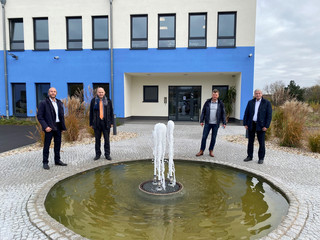 Vier Männer stehen vor einem Gebäude, verteilt um ein Wasserspiel.