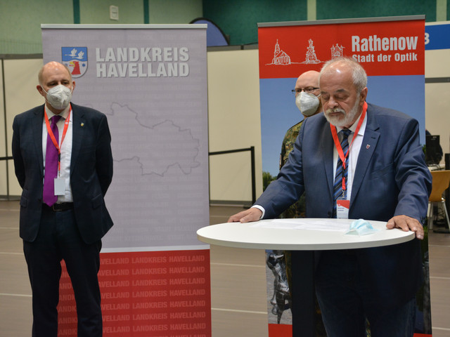 Bürgermeister Seeger steht an einem Stehtisch und hält eine Ansprache. Im Hintergrund stehen zwei weitere Männer und hören zu.