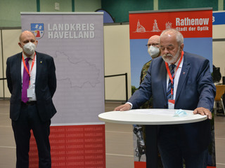 Bürgermeister Seeger steht an einem Stehtisch und hält eine Ansprache. Im Hintergrund stehen zwei weitere Männer und hören zu.