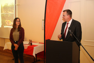 Johannes Funke steht am Rednerpult und hält die Laudatio. Preisträgerin Carolin Harras steht daneben und schaut zu ihm herüber.