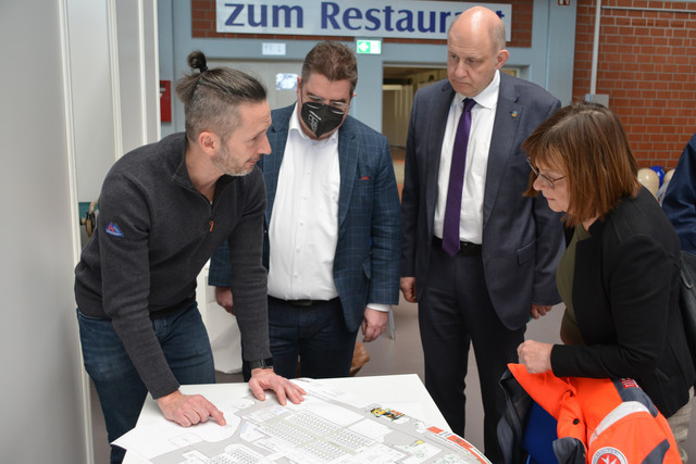 Vier Personen stehen um einen Tisch und schauen auf einen Lageplan.