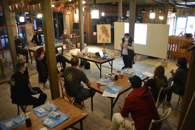 Eine Gruppe von Menschen sitzt in einem Raum. Eine Person steht vor der Gruppe und erklärt etwas.