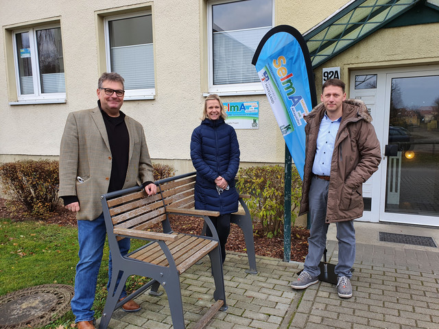 Drei Personen stehen vor dem Wohnblock, in dem sich die Musterwohnung befindet.