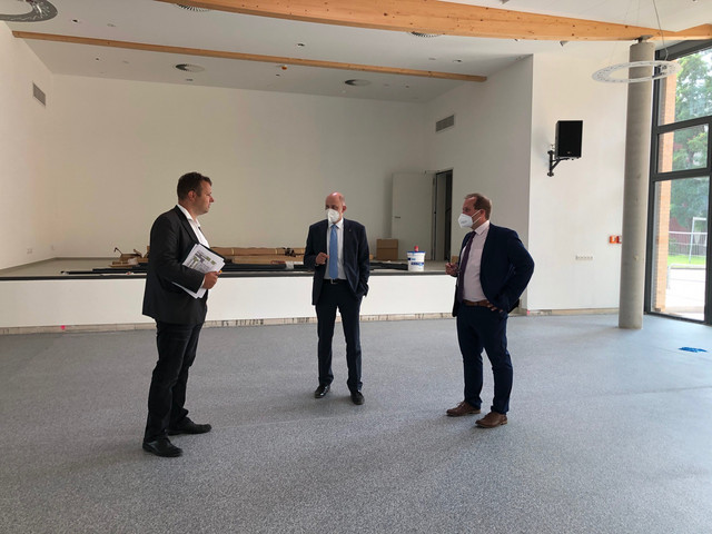 Drei Männer stehen im Halbkreis und unterhalten sich in der noch leeren neuen Halle.