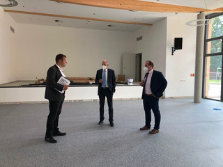 Drei Männer stehen im Halbkreis und unterhalten sich in der noch leeren neuen Halle.