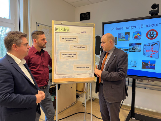 Drei Männer stehen vor einem Flipchart und unterhalten sich - Klick öffnet Bildbetrachter