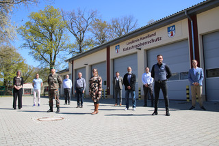 Die Mitglieder des havelländischen Corona-Krisenstabes stehen vor einer Fahrzeughalle.