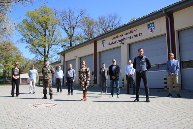 Die Mitglieder des havelländischen Corona-Krisenstabes stehen vor einer Fahrzeughalle.