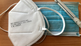 Auf einem Tisch liegen zwei Mund-Nasen-Bedeckungen sowie ein Corona-Test.
