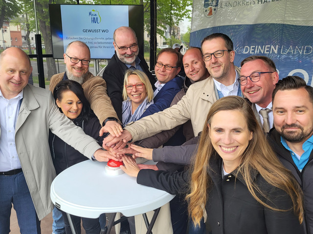 Der Landrat und Vertreter der havelländischen Kommunen stehen um einen Stehtisch und drücken den symbolischen Startbuzzer für die Landkreis-App - Klick öffnet Bildbetrachter