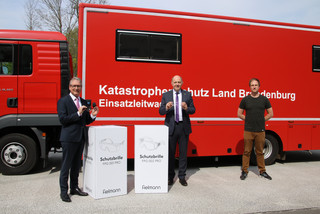 Harry Bräuer, Roger Lewandowski und Christoph Bajohr stehen vor einem Rettungsfahrzeug und zeigen zwei Schutzbrillen.
