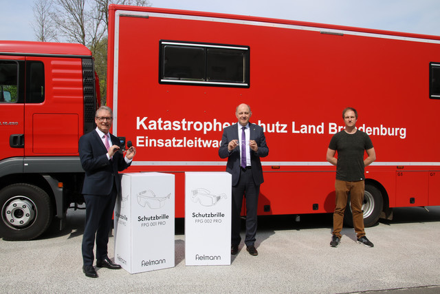 Harry Bräuer, Roger Lewandowski und Christoph Bajohr stehen vor einem Rettungsfahrzeug und zeigen zwei Schutzbrillen.