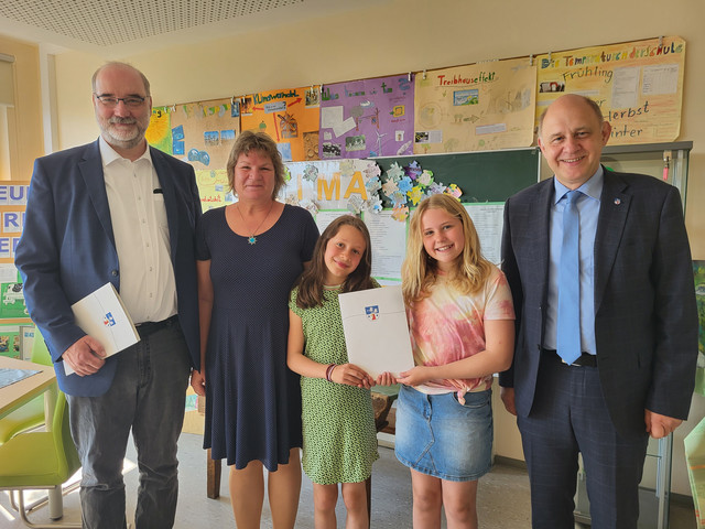 Fünf Personen stehen in einem Klassenraum, im Hintergrund die Tafel und Projektplakate an der Wand - Klick öffnet Bildbetrachter
