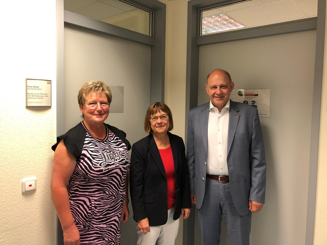 Drei Personen stehen in einem Flur vor einer Bürotür - Klich öffnet Bildbetrachter