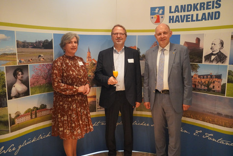 Der Landrat und die Kreistagsvorsitzende begrüßen die Gäste des Sommerempfangs vor einer Werbewand zum Landkreis Havelland - Klick öffnet Bildbetrachter