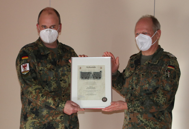 Oberstleutnant Klitscher steht links, Oberst Detlefsen steht rechts. Gemeinsam halten sie eine Urkunde hoch.