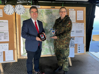 Zwei Personen stehen vor einer Pinnwand und halten getauschte Wappen in der Hand - Klick öffnet Bildbetrachter