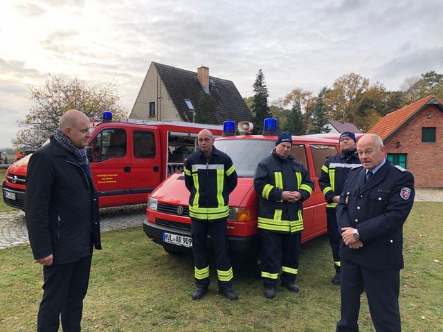 Zwei Personen stehen vor einem Feuerwehrfahrzeug und unterhalten sich.
