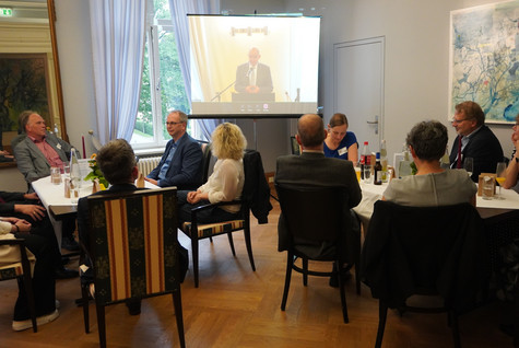 Blick in den Saal, wo die Gäste verteilt an mehreren Tischen sitzen und die Rede des Landrates an einem Bildschrim verfolgen - Klick öffnet Bildbetrachter