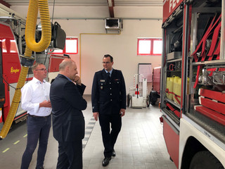 Drei Männer stehen neben einem Feuerwehrfahrzeug und reden miteinander.