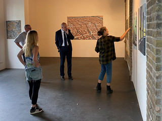 Eine Frau zeigt in einer Ausstellung auf ein Bild. Landrat Roger Lewandowski und zwei andere Personen schauen zu.