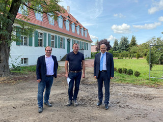 Drei Männer stehen vor dem Gutshaus und schauen in die Kamera.