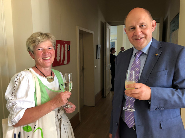 Eine Frau und ein Mann stehen mit einem Getränk in der Hand nebeneinander und schauen in die Kamera.