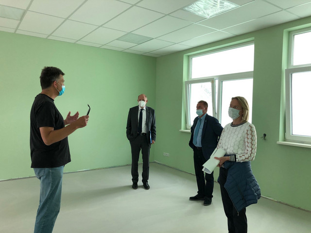 Vier Personen stehen in einem grün gestrichenen Raum und reden miteinander.