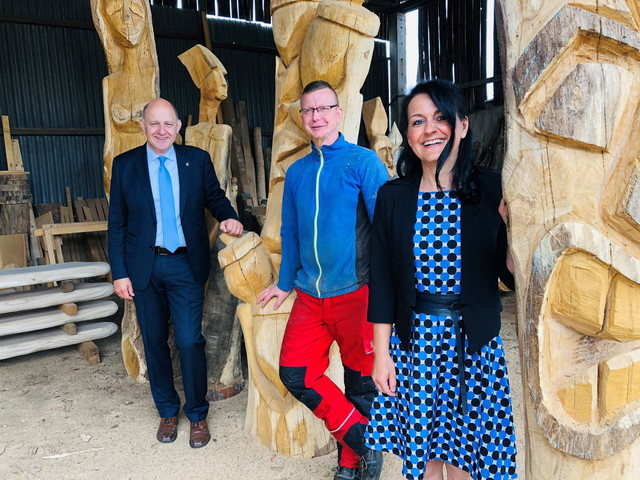 Drei Personen stehen zwischen großen Holzskulpturen - Klick öffnet Bildbetrachter