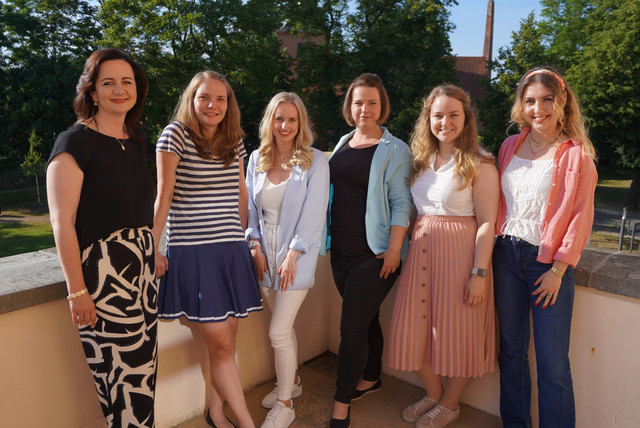 Eine Gruppe von Frauen steht nebeneinander auf einem Balkon und schaut in die Kamera.